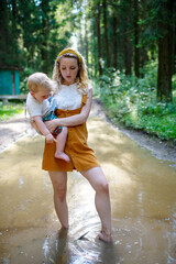 Wall Mural - Young mother holding her son and standing in the puddle in the forest