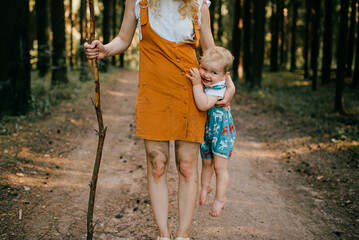 Wall Mural - Young mother with stick holding her son in the forest