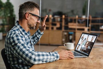 Wall Mural - Happy grey man waving hand while taking conference call on laptop