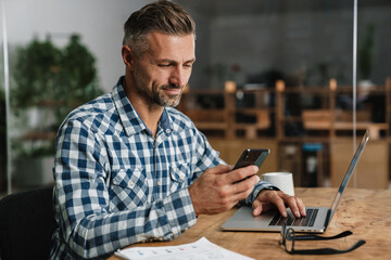 Wall Mural - Pleased grey man using mobile phone while working with laptop