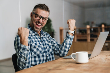Wall Mural - Excited man making winner gesture while working with laptop