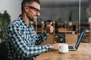 Wall Mural - Happy grey man showing thumb up while taking conference call on laptop