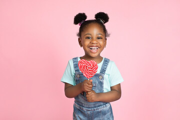 Happiness, childhood, kid and sweets. Cute pretty little African girl child, posing to camera with colorful lollipop in heart shape, and laughing