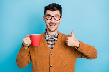 Poster - Photo of amazed brown haired man show thumb up hold cup wear plaid bow tie sweater isolated on blue color background