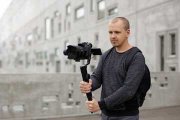 Wall Mural - hobby and creativity concept - professional videographer shooting video using modern dslr camera on 3-axis gimbal over grey concrete wall background