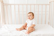 a baby boy six months old is sitting in his crib in a bright room