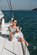 © Semachkovsky  - Free and lovely woman in a white dress and glasses, sitting on the edge of her expensive yacht with her legs down and enjoying the local view. Vacation concept.