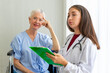 © ake - Caucasian old senior depressed upset woman patient on wheelchair talking to medical doctor with stethoscope  in hospital