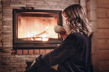 woman sitting by the fireplace with a cup of tea in her hands