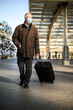 © Minerva Studio - Senior traveller walking outdoor with his trolley and wearing a protective mask against coronavirus pandemic