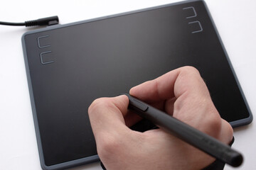 A person draws on a graphics tablet. The hand holds the touch pen. Wired graphic tablet for designer and artist. The man is working on a graphics tablet.