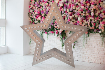 Decorative star with led retro lamp bulbs glowing. Big star with bulbs near wall with flowers. Star shaped white LED lights lamp single frame. Wedding decoration. Modern home interior decoration.