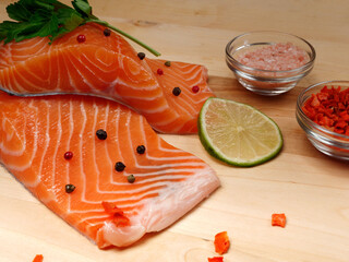 Close-up of two slices of red fresh raw salmon fillet with parsley and spices and lemon next to it. lie on a wooden cutting board. Healthy food concept