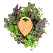 Cutting wooden board in the shape of a heart over various sweet basil herb leaves background. Healthy food concept. Top view with copy space.