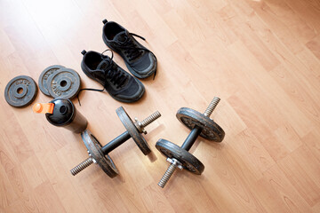 Dumbbells, bottle of water and sneakers on a wooden floor