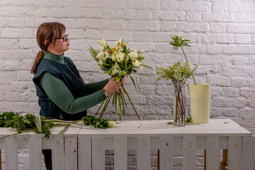 Florist workplace on the light background. The florist creates a floral arrangement of roses, lilacs, callas, carnations, hydrangeas, brasica, alstroemeria, ornithogalum, thuja and dracaena. Tutorial