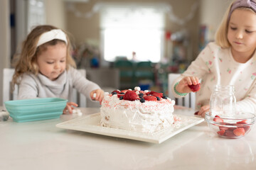 Two cute little girls in the kitchen decorating a cake