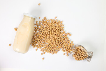 Soyabeans pouring from hart shape glass bottle around bottle of soya bean milk on white background