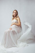 © satura_ - Elegant pregnant young woman standing wearing flying white fabric. Pregnancy, maternity and motherhood concept.