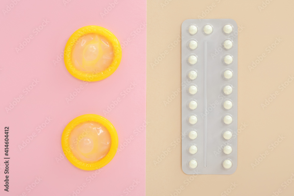 Open condoms and birth control pills on color background