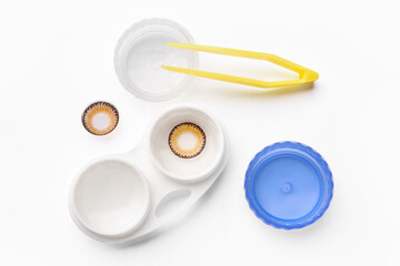 Tweezers, color contact lenses and container on white background