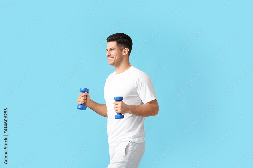 Sporty young man training with dumbbells on color background