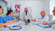 © DC Studio - Doctor discussing with medical staff in hospital conference room wearing lab coat. Clinic expert therapist talking with colleagues about disease, diagnosis for patients treatment issues