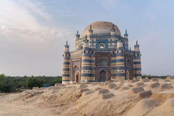 Landscape view of beautiful ancient medieval blue tomb of Bibi Jawindi with traditional graveyard in foreground in Uch Sharif, Bahawalpur, Punjab, Pakistan