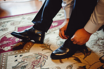 A man puts on classic lacquer shoes. The bride with a cool cloth laces shoes