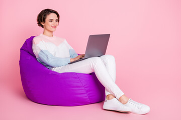 Poster - Full length photo portrait of woman working on laptop sitting in violet beanbag chair isolated on pastel pink colored background