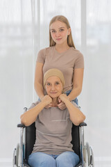 Wall Mural - A young and beautiful grateful daughter helping to arrange head scarf to encourage her mother's cancer patient on wheelchair and fortifies her to fight during the chemotherapy