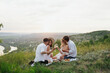 © eduard - Group of four young friends enjoying a healthy picnic sitting outdoors on the hill drinking white wine and eating a variety of fresh fruit.