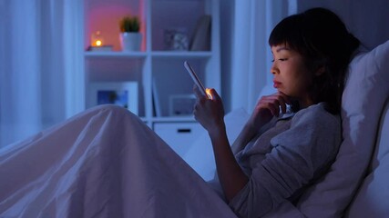 technology, internet and people concept - young asian woman with smartphone lying in bed at home at night