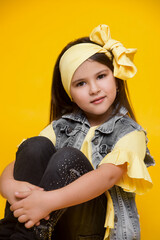 Children's portrait. Close-up girl in yellow clothes and a gray denim jacket on a bright yellow background smiles, folded her arms. Expressive eyes. sits