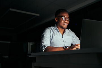 smiling african young businessman working overtime in the office to finish the project within the de