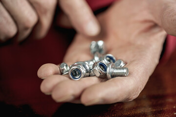 Steel bolts and nuts on wrinkled hand of old man to calculate right number