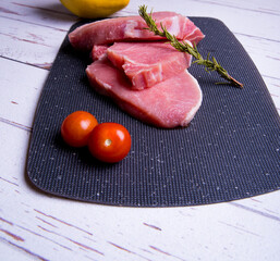 Pork. Fresh pork steaks on a black chopping board and spiced, cherry tomatoes, rosemary, peppercorns, quince, copy space