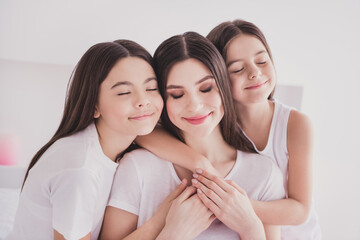 Wall Mural - Photo of charming dreamy three siblings nightwear sitting bed smiling embracing closed eyes indoors inside room home