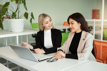 two beautiful young women in the office at the table with a laptop 