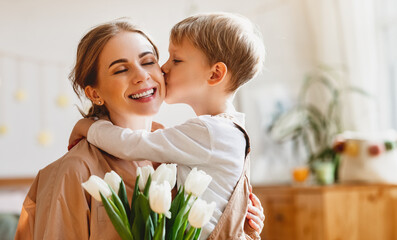 tender son kisses the happy mother and gives her a bouquet of tulips, congratulating her on mother's