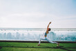 © BullRun - Woman taking Warrior pose on top of big building in sunny day