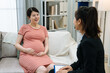© PR Image Factory - Young maternity lady with big belly and businesswoman discussing life insurance agreement. confident female agent sales in formal suit talking and explaining contract to pregnant woman patient.