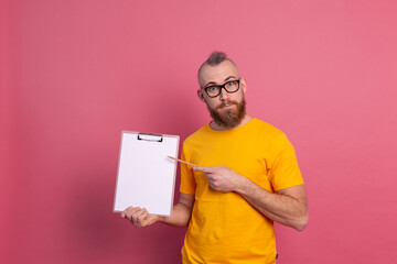 Smiling bearded man wearing eyeglasses wearing casual clothes holding a clipboard with a blank paper pointing