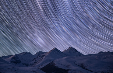 Wall Mural - Night winter landscape, the snow-capped mountains under the colorful star trails on the sky. Night time lapse photography.