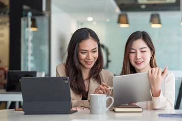 Two Asian beautiful woman consult a collaboration structure using a tablet at the office.