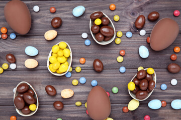 Wall Mural - Easter chocolate eggs with candies on brown wooden table