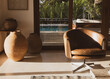 © EZ PHOTOS - Modern luxury summer holiday or vacation beach house living room interior with rustic ceramic clay vases and armchair on the foreground and view of the swimming pool through the glass door.