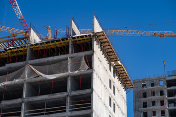 Construction of a tall building, several construction cranes and scaffolding on a blue sky background, background