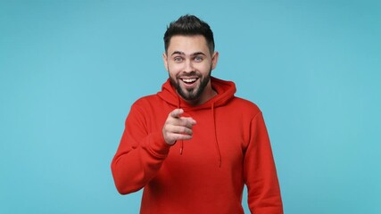 Wall Mural - Excited funny young man 20s in red streetwear hoodie isolated on blue background studio. People lifestyle concept. Pointing finger camera on you waving meeting greeting with hand as notices someone