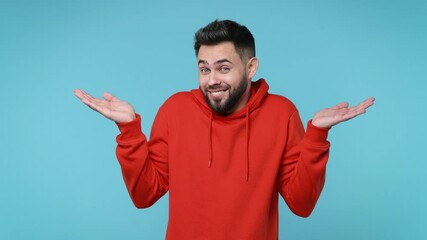 Wall Mural - Confused puzzled bearded young man 20s years old in casual red streetwear hoodie isolated on pastel blue color background studio. People sincere emotions lifestyle concept. Spreading hands say oops